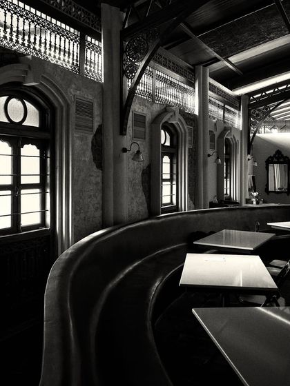 A long, curved banquette provides seating along the wall, punctuated by arched windows that bring in natural light.