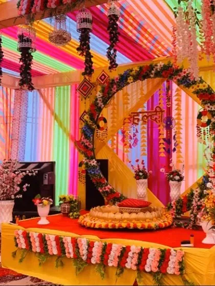 This is a very colorful haldi stage I put together. It features a rainbow of fabric drapes on the ceiling and a floral arch around the main seating area, which includes a traditional urli for the ceremony.