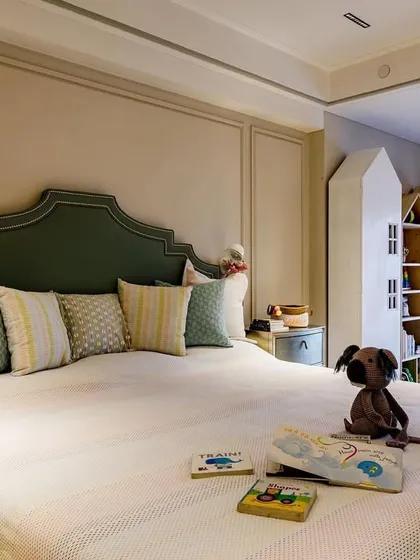 This toddler's room is designed to be a dreamy and restful space. The custom-shaped upholstered headboard in a soft green adds a touch of elegance, while the house-shaped bookshelves provide a fun place for toys and books.