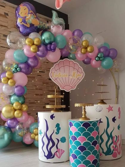 A compact and charming mermaid-themed setup. This decoration uses a golden ring with a balloon arch, themed pedestals with scale patterns, and a custom seashell sign to bring the magic of mermaids to any space.