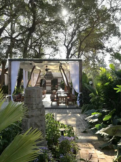 An outdoor dining area at Sanctuary Bar, set under a canopy and draped with white curtains. The space feels light and airy, offering an elegant dining experience surrounded by the lush Goan landscape.