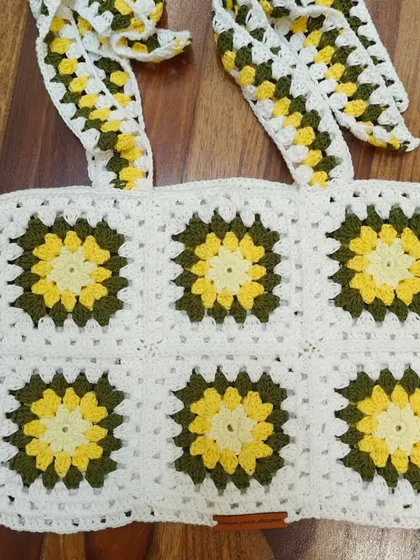 A flat-lay of the sunflower granny square top, showing the construction and the adjustable tie-straps. The design is centered around six beautiful sunflower motifs.
