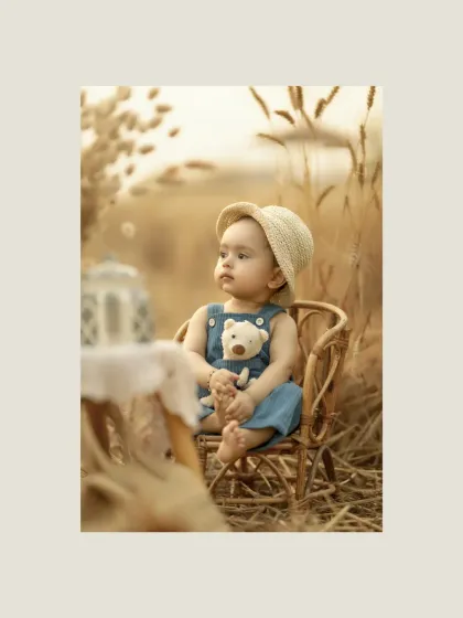 Here, a little one sits peacefully in a golden wheat field, holding his teddy bear. This outdoor portrait, taken during the beautiful golden hour, uses the warm, soft light to create a serene and nostalgic atmosphere, connecting the innocence of childhood with the nurturing spirit of nature.