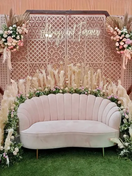 This pastel-themed photo booth features a "Always and Forever" neon sign against a lattice backdrop. The pampas grass and blush pink sofa add a touch of modern, bohemian flair.