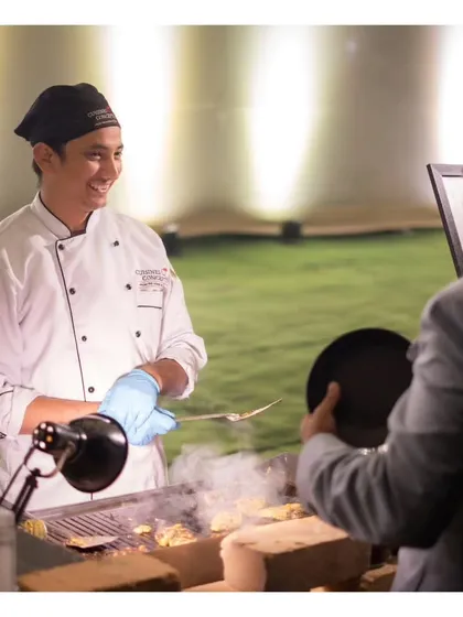 A smiling chef interacts with a guest while serving from a live grill. This image perfectly captures the friendly and professional service that accompanies our delicious food.