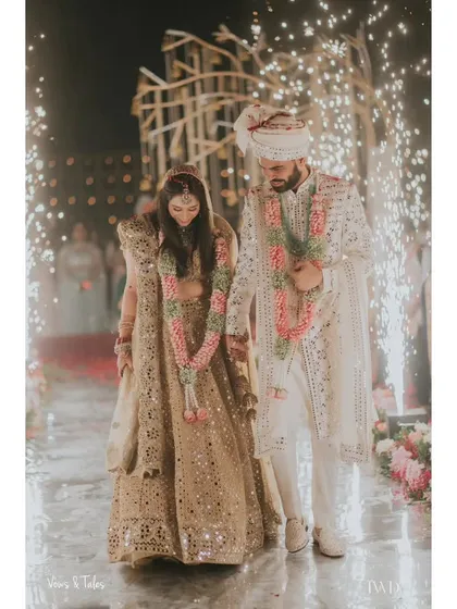 A moment of quiet connection amidst the grand celebration. The couple walks hand-in-hand, framed by the sparks of cold pyros, their path illuminated as they begin their life together.