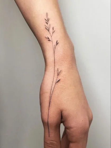 A delicate sprig of wheat tattooed along the side of the hand and wrist. This fine-line piece is elegant and natural, flowing beautifully with the body's curves.