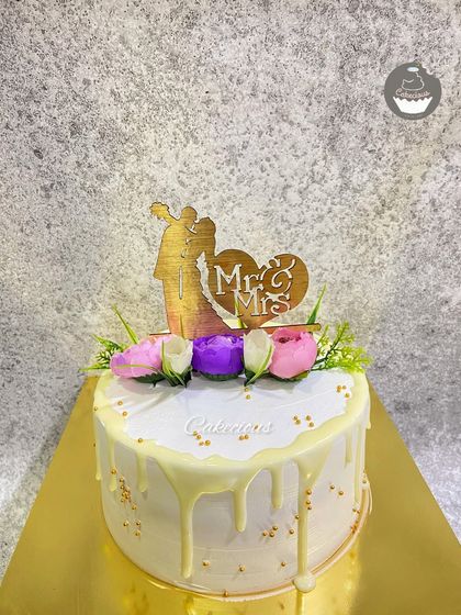 A classic Mr. & Mrs. wedding cake. The white drip and floral toppers create a simple, elegant look for the special day.