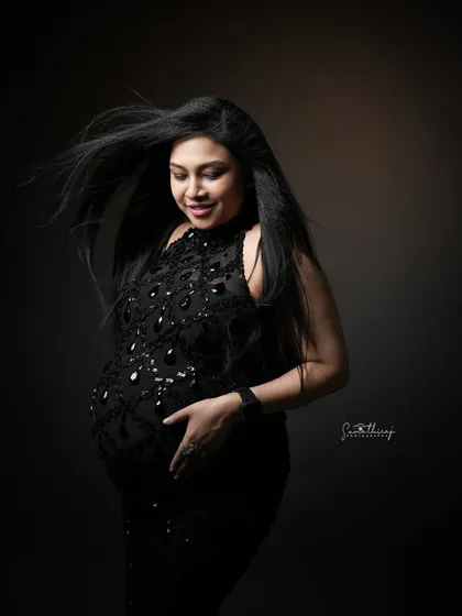 A stunning portrait of a mother-to-be in a black sequined gown with her hair blowing in the wind. The dramatic lighting and movement create a dynamic and glamorous shot.