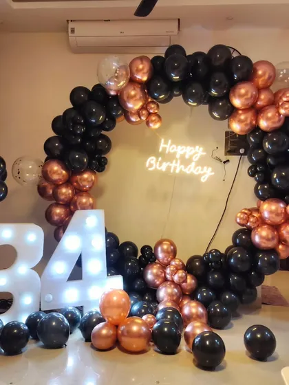 A stylish 34th birthday party with a black and rose gold theme, featuring a full circular balloon arch and large light-up marquee numbers.