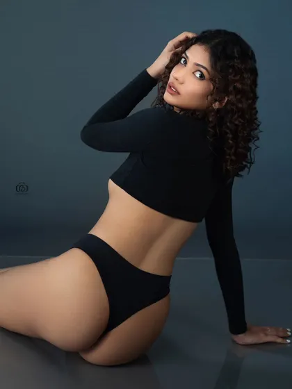 A low-key studio shot that plays with shadows and form. The model's pose and the simple black attire are highlighted by a single light source, creating a sense of intimacy and focusing on the human form.