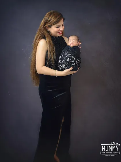 A stunning portrait of a mother in a sleek black dress holding her sleeping newborn. This shot is elegant and timeless, focusing on the beauty of motherhood.