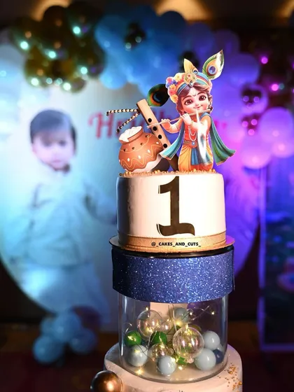 A close-up of the Krishna-themed cake, showing the beautiful details of the topper and the clear tier filled with lights.