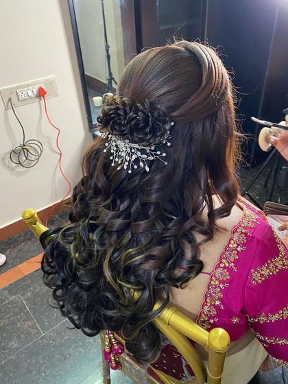 A reception hairstyle with defined curls and highlights, styled into a half-updo with a braided detail and a sparkling silver accessory.