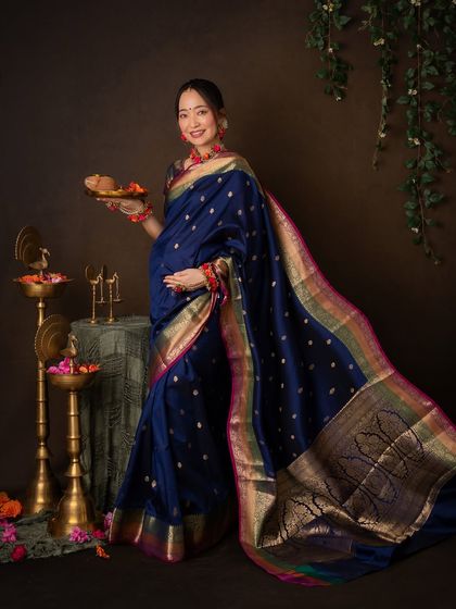 A full-length portrait showcasing the magnificent drape and border of the silk saree. She holds a plate with diyas, symbolizing light and life.