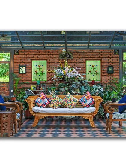A vibrant seating area in a glass-enclosed veranda at Magnolia Resorts. The exposed brick wall, colorful cushions, and surrounding plants create a cheerful and eclectic space that feels like a tropical conservatory.