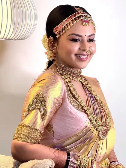 A bride in a pink and gold Kanchipuram saree. Her custom blouse features unique embroidery on the sleeves and a flattering neckline, designed to complement her traditional jewelry.