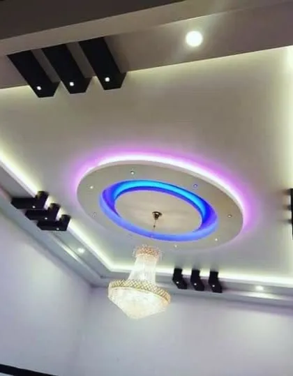 This ceiling combines a central circular element with multi-colored LED lighting and a modern chandelier. It proves that you can have both a fan and a stunning false ceiling.