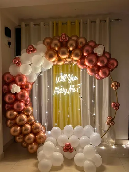 A simple yet beautiful proposal setup in your home. This circular arch with rose gold and white chrome balloons, paired with a "Will You Marry Me?" neon sign, creates the perfect backdrop for asking the big question.