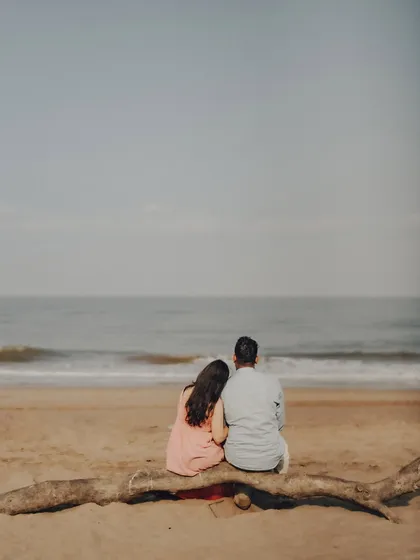 A quiet, reflective moment for Anushka and Manu, sitting on driftwood and looking out at the sea. This wide shot captures the serene beauty and scale of a beach location.