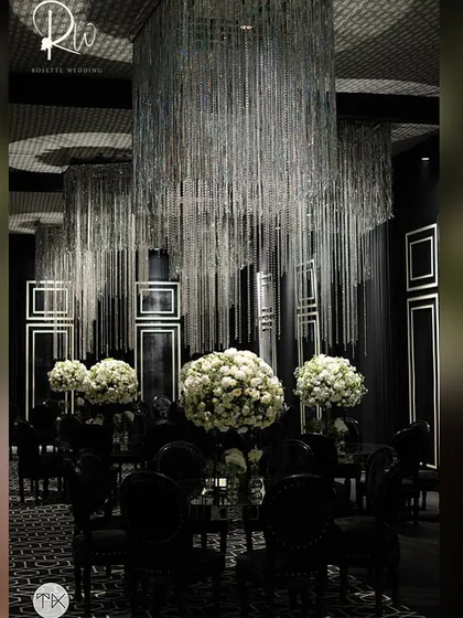An all-black dining setup with large white floral centerpieces and silver tassel chandeliers, creating a high-contrast, glamorous look.