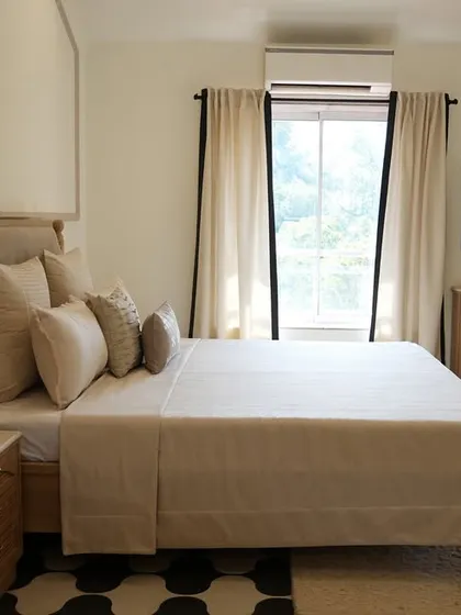 This view of the Alibaug master bedroom showcases the custom wooden furniture and the striking black and white geometric flooring. The design balances classic elegance with modern graphic elements.