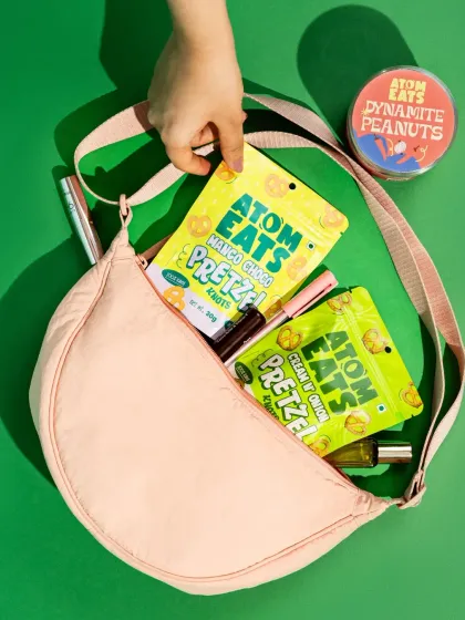 An overhead shot of a handbag with Atom Eats pretzel packs inside. This lifestyle image positions the snack as a convenient, on-the-go option for a modern consumer.