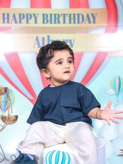 A classic portrait of the birthday boy at his hot air balloon themed first birthday. The decor, featuring a miniature ferris wheel and balloon backdrop, provides a beautiful setting for timeless photos.