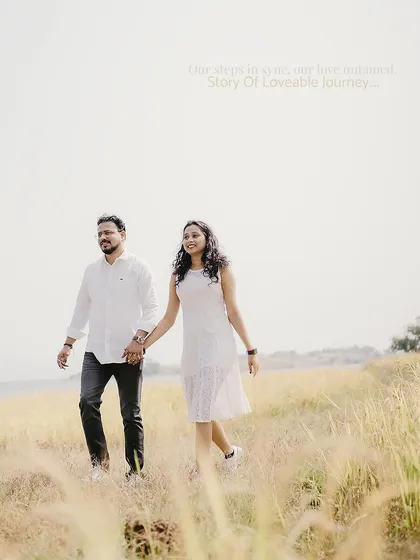 A bright and happy shot of a couple in modern-casual white outfits, walking through a sunlit field.