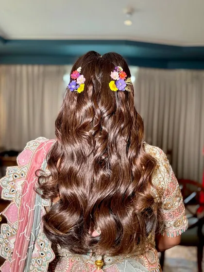 The hairstyle featured soft, bouncy curls, half-tied and decorated with colorful flowers to match the embroidery on her lehenga.