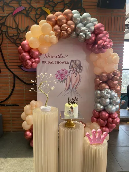 A chic and modern bridal shower setup. This design features a stylish balloon arch in metallic and pastel tones, a personalized backdrop, and elegant plinths for the cake and decorative props.