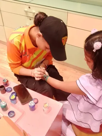 A staff member carefully paints a design on a child's hand. Our face and hand painting station is a popular addition to parties and events.