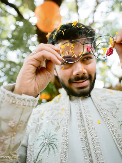 A playful portrait of the groom, his glasses covered in flower petals, capturing the fun and messy spirit of the Haldi ceremony.