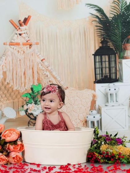 A smiling baby girl enjoys her bath in a beautiful bohemian-themed setup. The mix of flowers, lanterns, and natural textures makes this a unique and artistic portrait.