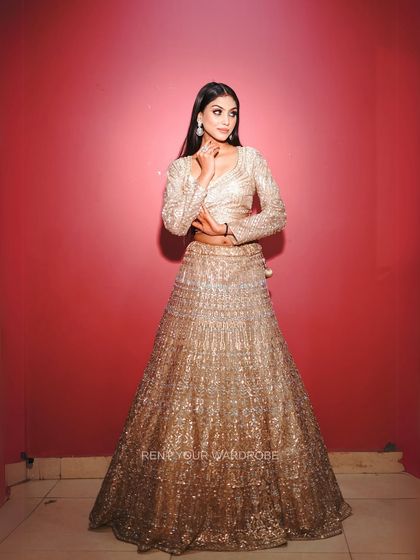 A full-length shot of the golden lehenga against a contrasting red background, making the outfit shine.