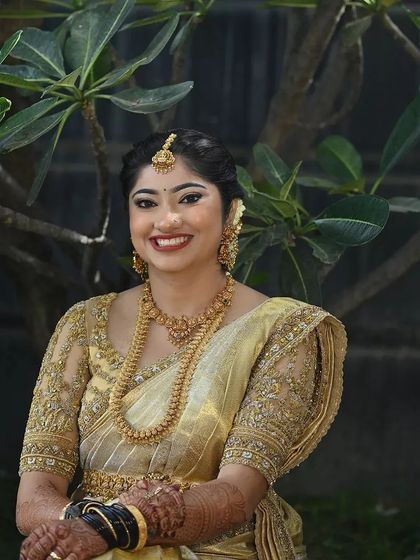 A smiling bride in her shimmering gold saree. The fully embroidered blouse and classic gold jewelry create a look that is both traditional and incredibly glamorous.