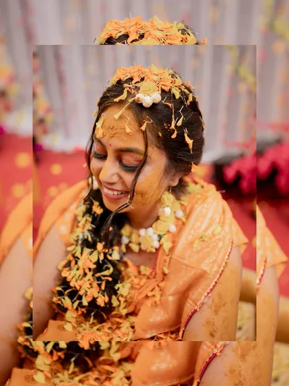 A happy bride covered in turmeric and flower petals, smiling with her eyes closed, completely enjoying her Haldi ceremony.