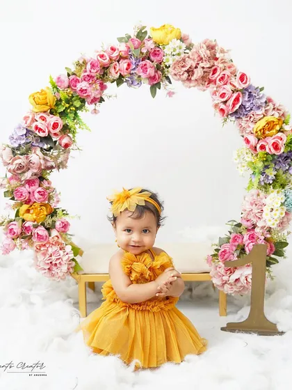 A floral fantasy for a first birthday. This baby girl is sitting in front of a beautiful arch of colorful flowers, creating a vibrant and joyful portrait.