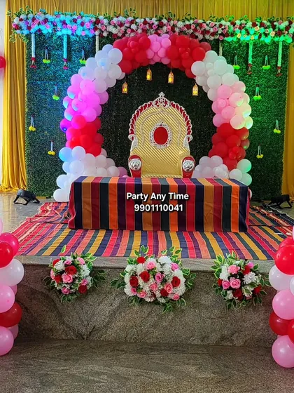 A decoration for a traditional function, combining a balloon arch with a green foliage backdrop and floral arrangements.