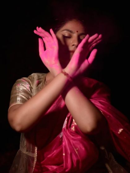 An expressive portrait with hands crossed, veiled by pink Holi color. This image captures a moment of inner connection amidst the external celebration.