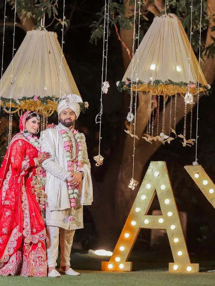 The newlywed couple poses against a beautifully lit backdrop. This image showcases the stunning wedding decor and the couple's coordinated, regal outfits.
