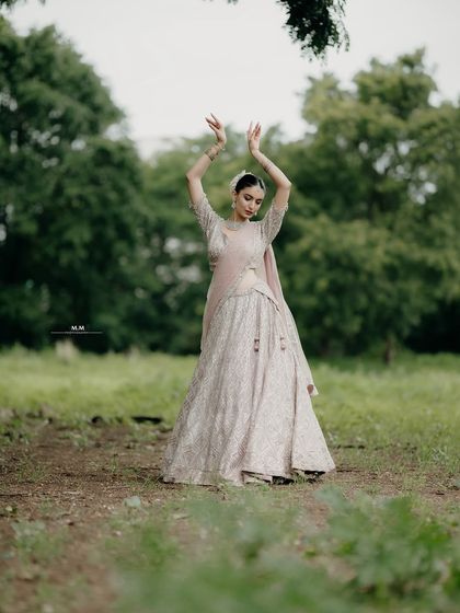 A graceful dance pose in the middle of a field. This artistic shot showcases the bride's elegance and the flowing beauty of her lehenga.