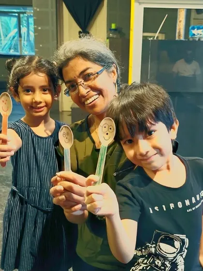 Fun with spoon puppets! A facilitator and two young students proudly display the simple yet expressive puppets they created in a workshop. Creativity can be found in the simplest of objects.