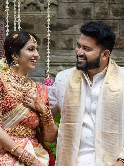 A couple shares a loving look against a backdrop of rustic stone walls and lush greenery.