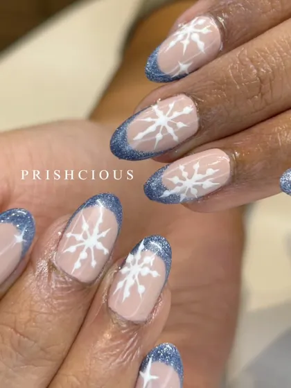 Jingle all the way with these winter wonderland nails. This design features a glittery blue French tip on natural-length nails, decorated with hand-painted white snowflakes.