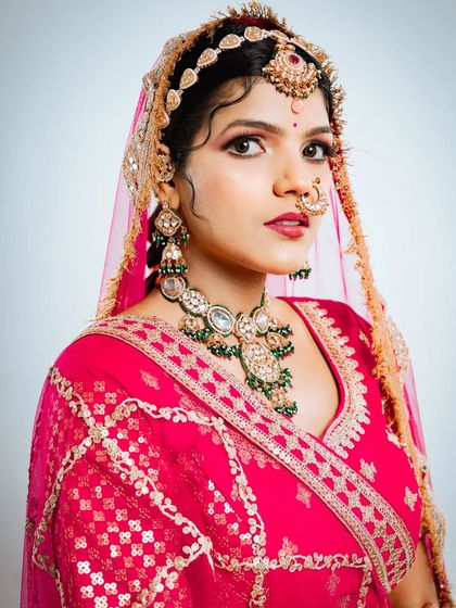A close up portrait showcasing the heavy green and white stone necklace, nath, and maang tikka that complete this traditional Rajasthani bridal look.