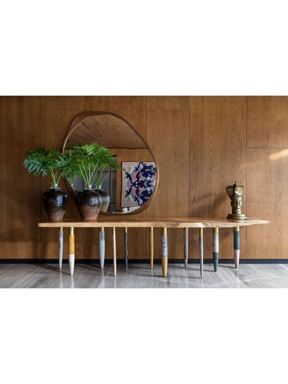 A detail of the K Residence lobby, featuring a console with a solid wooden top and beautifully crafted monolithic marble legs. Above it, a sculptural brass mirror reflects the art and architecture of the space.