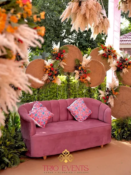 A closer look at the bridal sofa, highlighting the contrast between the soft pink velvet and the rustic, natural backdrop. The printed cushions add a pop of pattern and color.