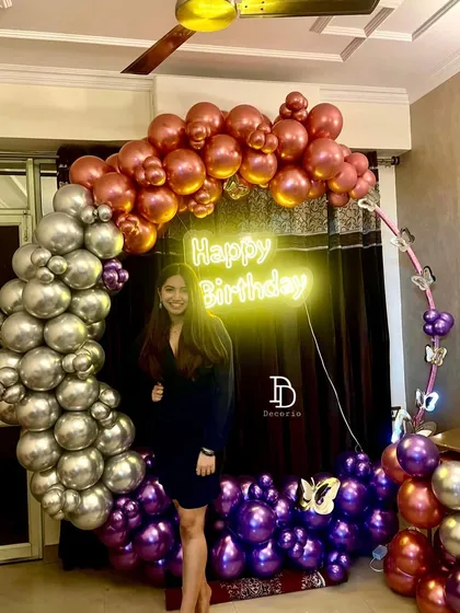 The birthday girl enjoying her custom-decorated party space. The circular balloon arch in metallic shades of purple, silver, and rose gold creates a beautiful frame for photos.