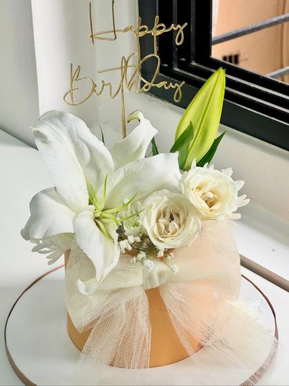 Where simplicity blooms into elegance. This minimal floral birthday cake is crafted with soft whites, pure textures, and a bouquet of fresh lilies and roses for a touch of timeless grace.